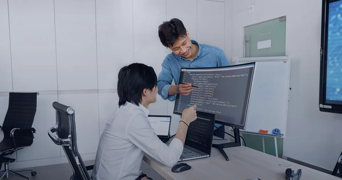 Two developers reviewing code together on a large monitor